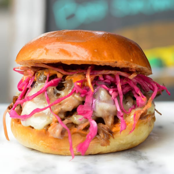 A pulled pork sandwich from The Sandwich Shop, topped with melted cheese and vibrant pink pickled cabbage.