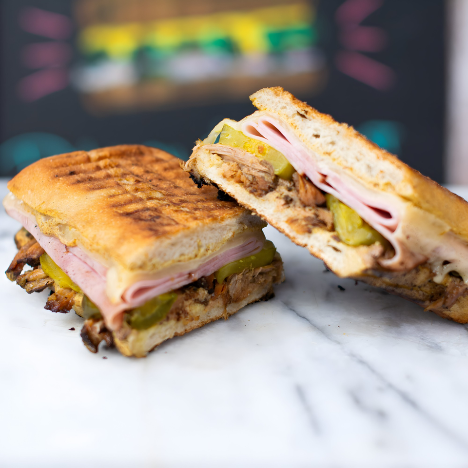 Two halves of a grilled Cuban sandwich with ham, pork, cheese, and pickles on a marble surface.