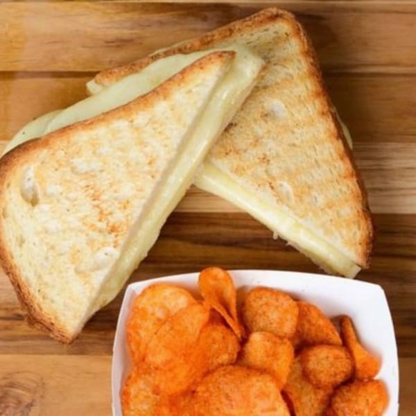 Two grilled cheese sandwiches with melted cheese and a side of orange chips on a wooden board.