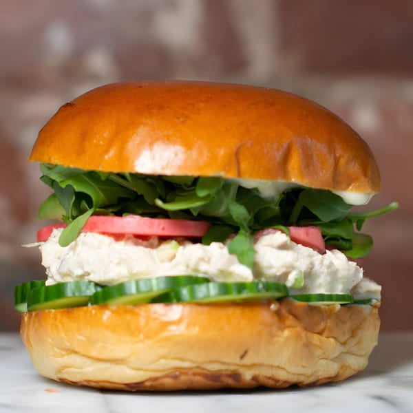 Chicken salad sandwich on a brioche bun with arugula, tomato, and cucumber slices.
