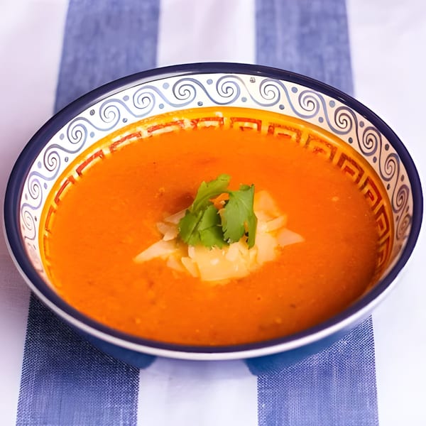 A bowl of tomato soup with shredded cheese and cilantro on a blue and white striped tablecloth.