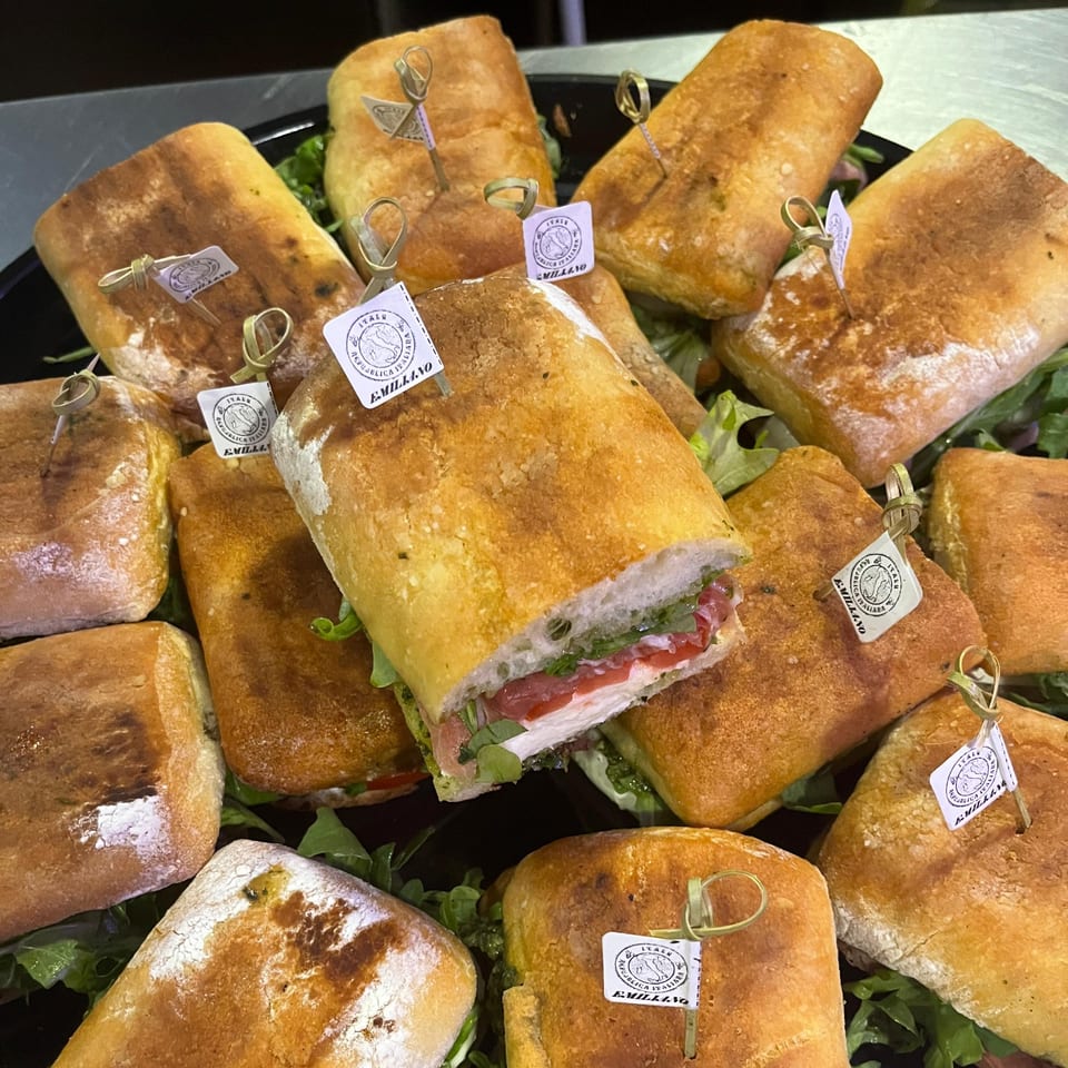A platter of ciabatta sandwiches, one cut open to reveal turkey, prosciutto, and greens.