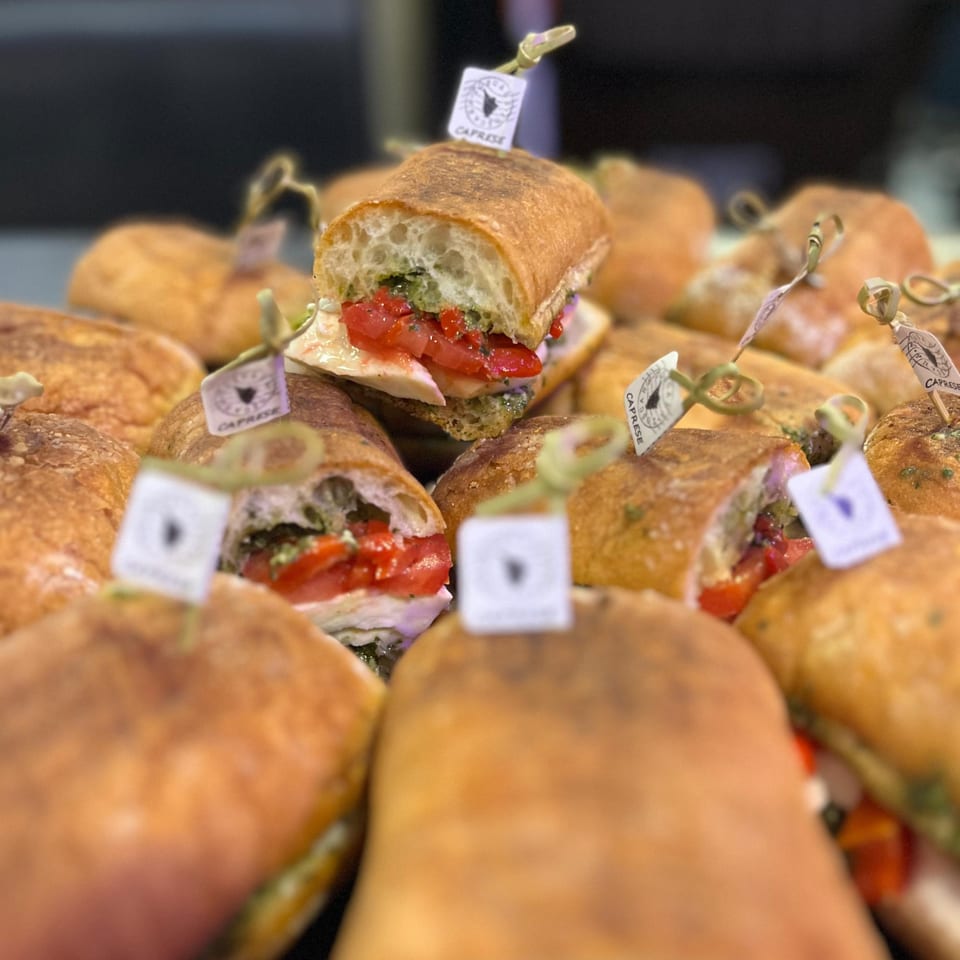 Close-up of multiple Caprese sandwiches from The Sandwich Shop, with pesto, tomatoes, and cheese.