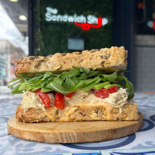 A chicken salad sandwich with red peppers and arugula on multigrain bread, on a wooden board.