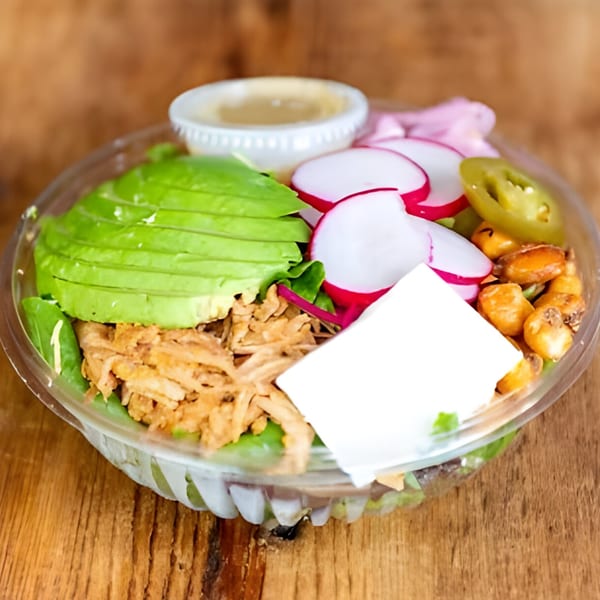A colorful salad bowl with avocado, pulled pork, radishes, corn, and jalapeños.